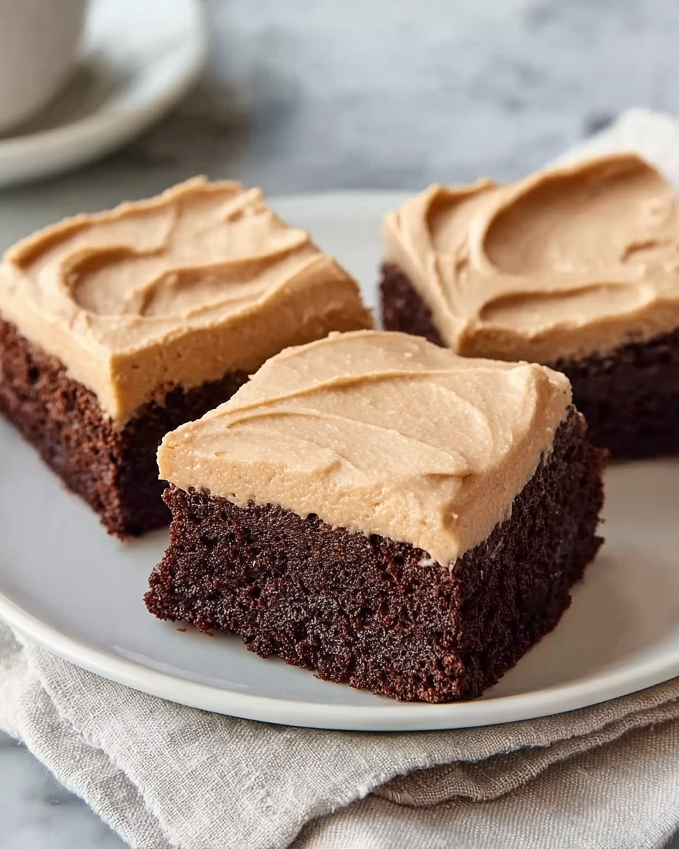 Three squares of chocolate cake with a thick, smooth light brown frosting layer on top are placed closely together on a white plate. The chocolate cake layer is dense, moist, and dark brown with a slightly crumbly texture visible at the sides and bottom. The frosting is evenly spread with soft swirls and a creamy texture, covering the entire top of each piece. The plate sits on a white marbled surface with a soft white cloth nearby. Photo taken with an iphone --ar 4:5 --v 7