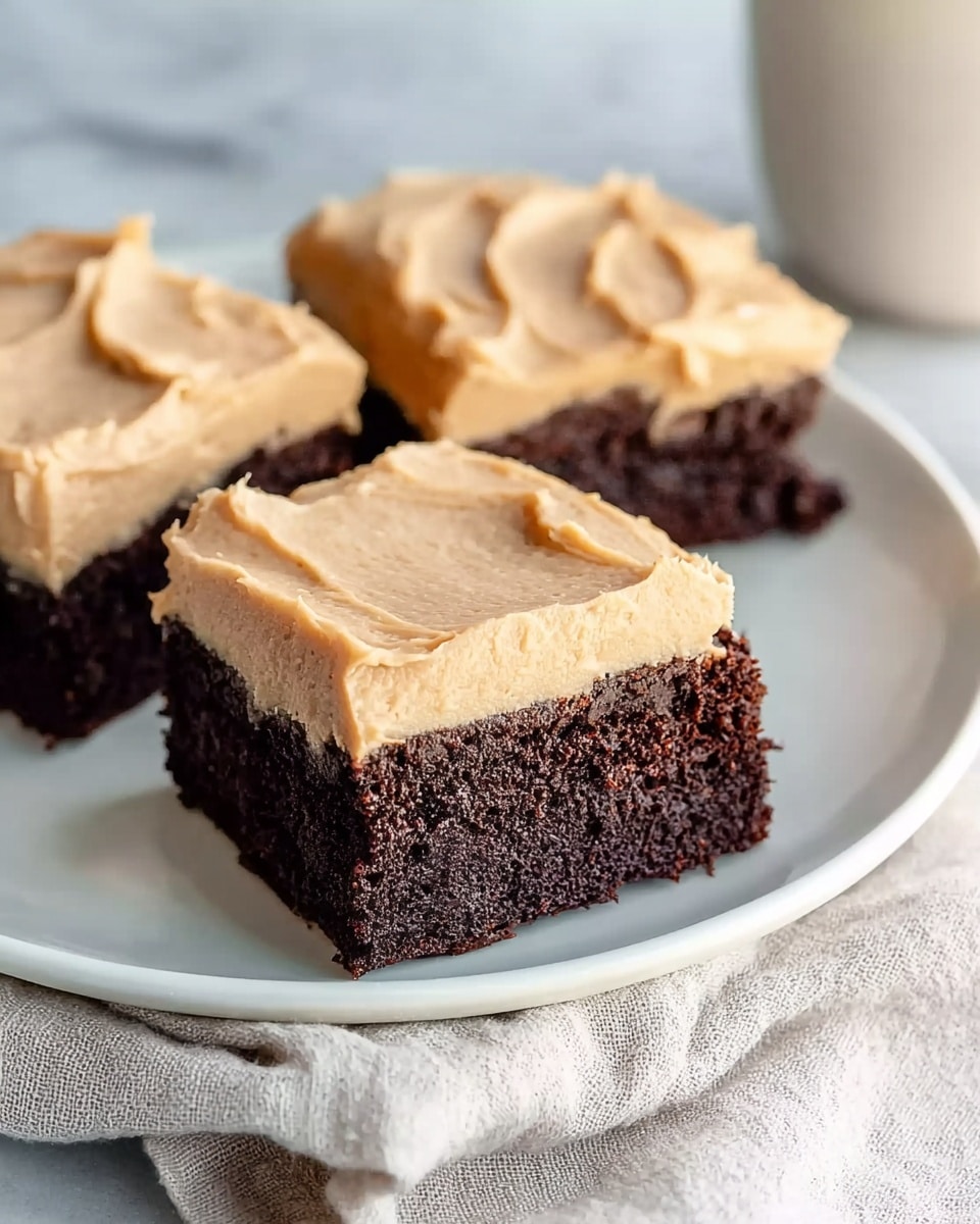 Three square brownies are placed close together on a white plate, each with one thick, even layer of light tan frosting spread smoothly on top. The brownies have a dense, rich dark brown base with a slightly crumbly texture, and the frosting looks creamy with soft swirls. The plate rests on a white marbled surface with a soft cloth partly visible underneath. The overall look is simple and inviting, showing a clear contrast between the dark brownie and the light frosting. Photo taken with an iphone --ar 4:5 --v 7