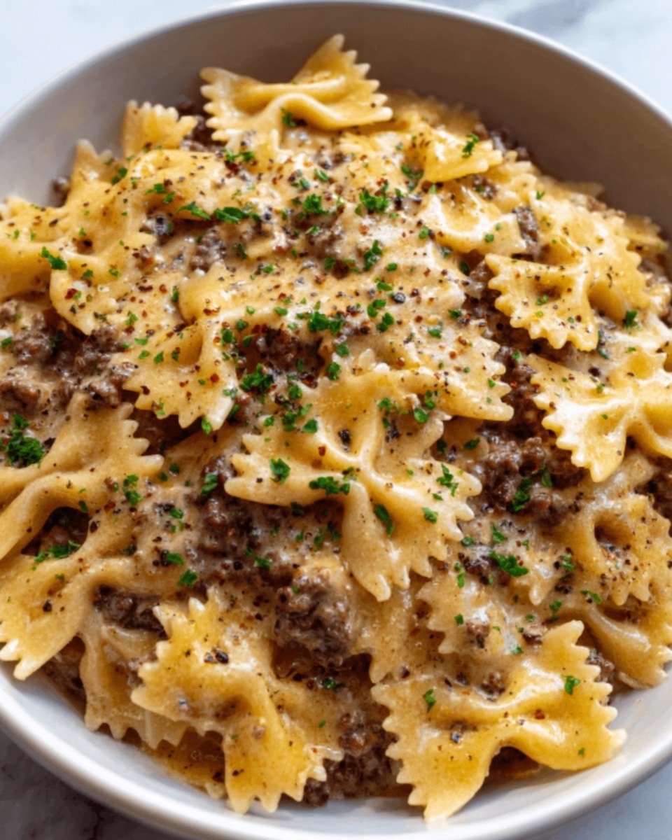 The image shows a bowl filled with farfalle pasta layered with ground meat sauce. The farfalle pasta is light yellow, each piece bow-shaped with slightly rough texture. The ground meat sauce is brown and spread evenly among the pasta, creating small pockets of meat. The dish is topped with finely grated cheese that adds a creamy white layer, lightly melting into the sauce. Small pieces of green herbs are sprinkled on top, adding color contrast. The bowl is white and set on a white marbled surface. Photo taken with an iphone --ar 4:5 --v 7