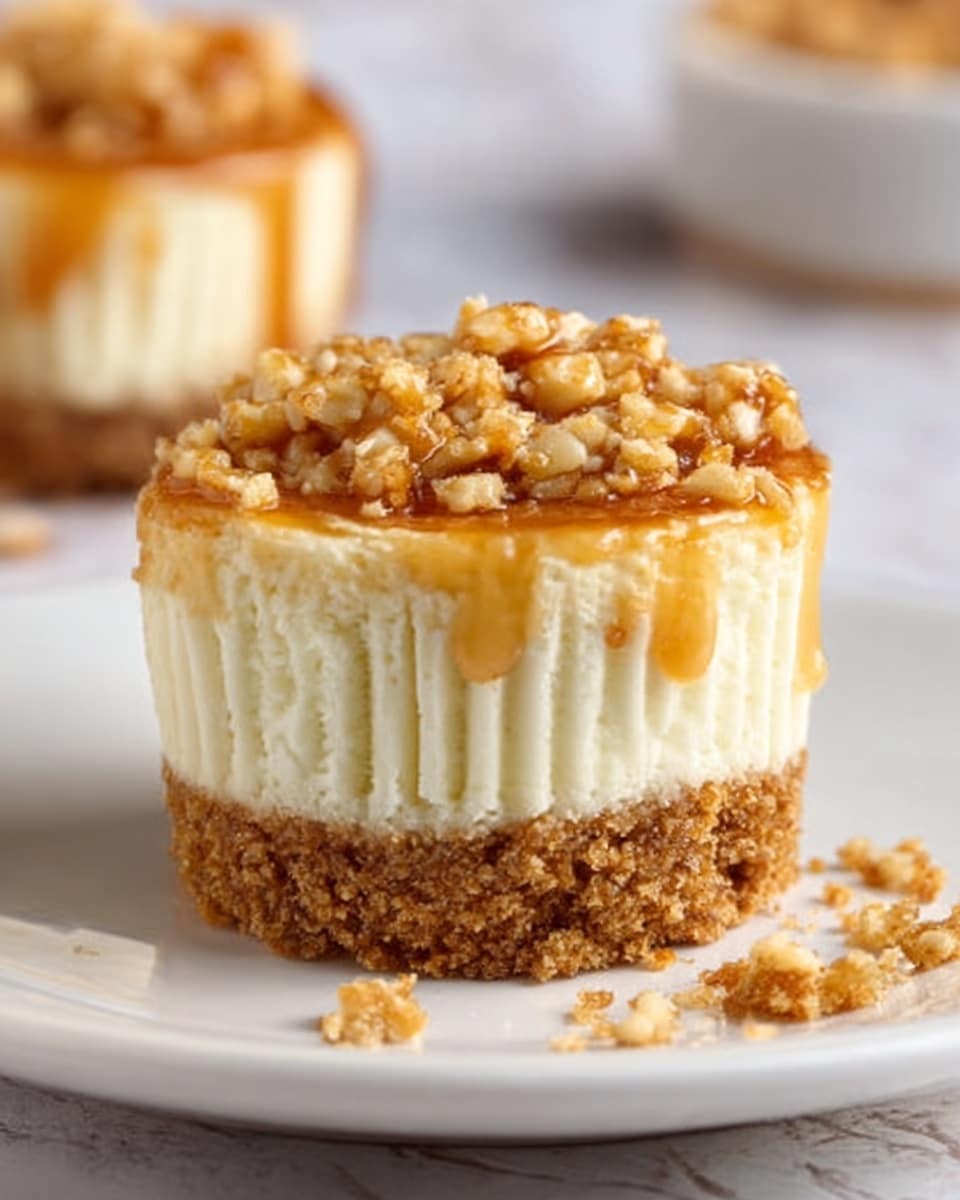 A small cheesecake cup is shown on a white plate with a few crumbs around it. The cheesecake has three layers: a thick golden brown crumbly base, a smooth white creamy middle, and a light golden crumb topping. A drizzle of shiny caramel sauce flows over the sides and top of the crumb layer, making it look sticky and sweet. The background is a white marbled surface. Photo taken with an iphone --ar 4:5 --v 7
