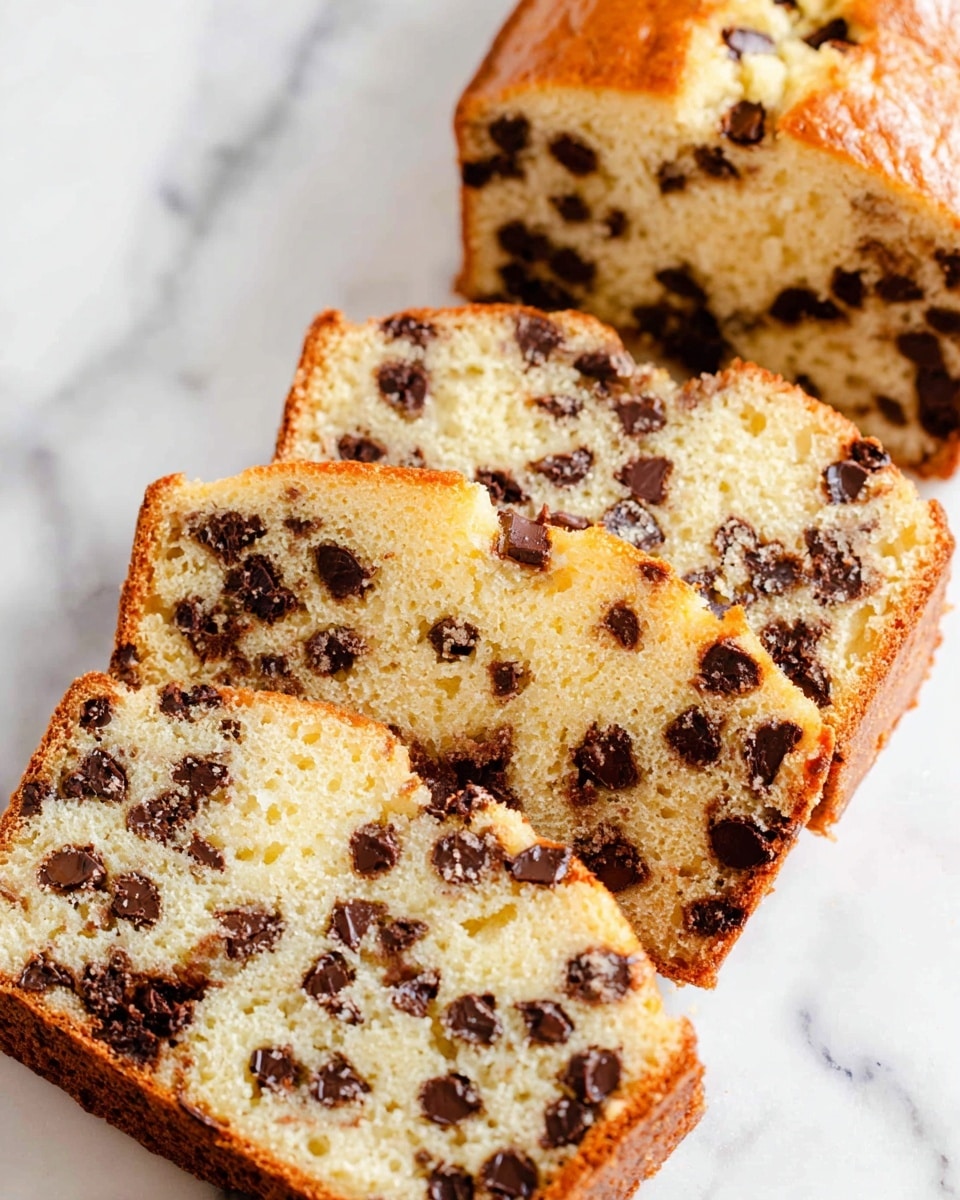 A close-up view of three thick slices of chocolate chip bread stacked slightly overlapping on a white marbled surface. The bread has a soft, light golden brown crust with a tender, pale yellow interior filled with many dark chocolate chips scattered evenly throughout. The texture inside looks moist and crumbly with small air pockets visible, while the chocolate chips add a rich contrast with their deep brown color and smooth, slightly glossy appearance. Photo taken with an iphone --ar 4:5 --v 7
