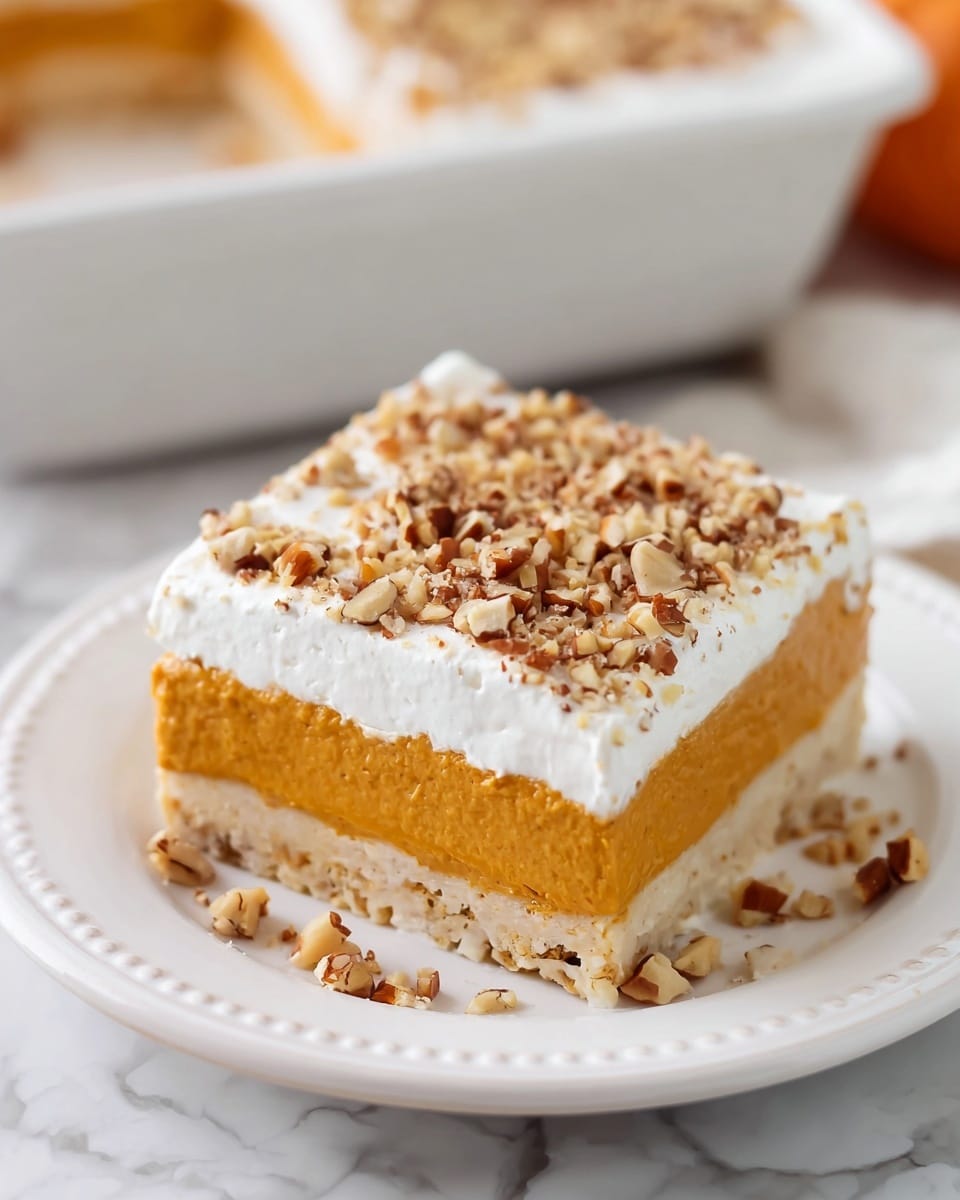 A slice of dessert is shown on a white plate with a dotted rim, placed on a white marbled surface. The dessert has three layers: the bottom layer is a light brown nutty crust with visible nut pieces, the middle layer is a smooth orange pumpkin-colored filling, and the top layer is a thick, white cream topped evenly with chopped nuts. Some chopped nuts are scattered on the plate around the dessert. In the background, a white dish with more of the dessert is slightly out of focus. Photo taken with an iphone --ar 4:5 --v 7