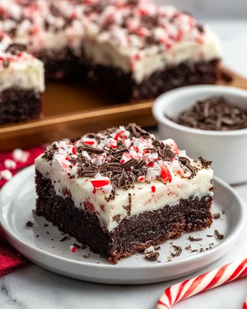 The image shows a close-up of a dessert square placed on a small white plate on a white marbled surface. The dessert has three main layers: a thick, dark brown chocolate brownie base, topped with a creamy white layer that looks smooth and soft, and finished with a sprinkle of crushed red and white peppermint candy pieces along with small dark chocolate shavings scattered on top. The texture of the brownie looks rich and dense, while the creamy layer is even and shiny. In the background, more dessert squares are visible, slightly blurred, and a small white bowl filled with dark chocolate shavings is placed nearby. A red and white striped candy cane lies on the surface in front. photo taken with an iphone --ar 4:5 --v 7