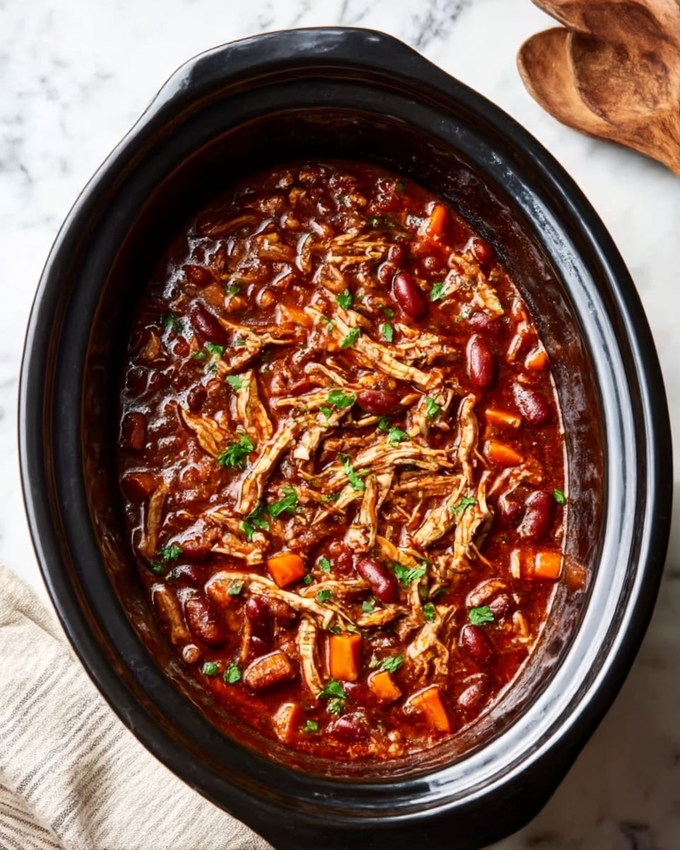 The image shows a black slow cooker filled with a rich, dark brown stew. The stew has shredded pieces of chicken on top, mixed with small chunks of red bell pepper and kidney beans. The surface is garnished with fresh green herbs scattered around, adding a touch of color. The slow cooker is placed on a white marbled surface with a striped cloth beside it. photo taken with an iphone --ar 4:5 --v 7