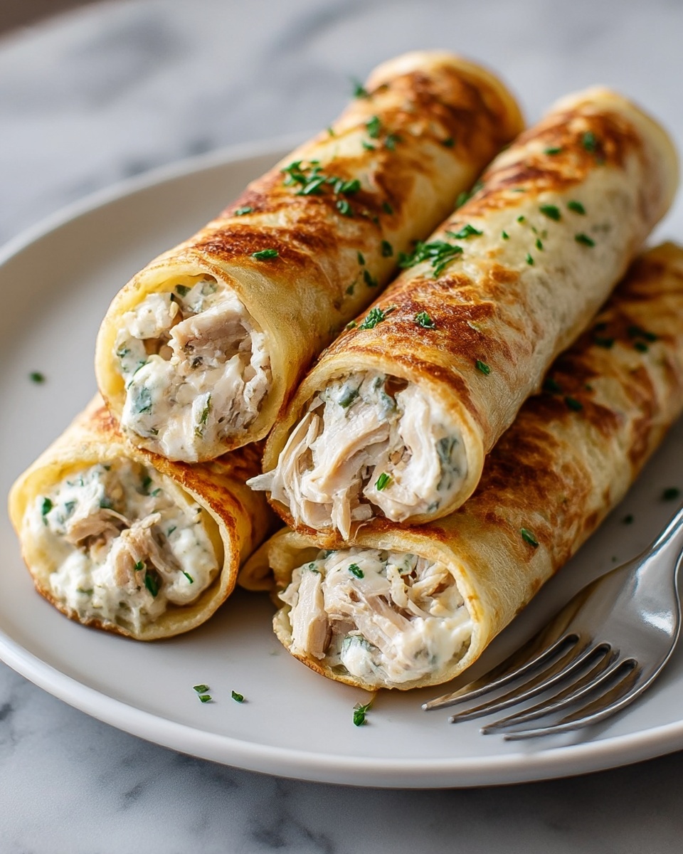 The image shows four rolled crepes placed closely side by side on a white round plate. Each crepe has a golden brown, slightly crispy outer layer with scattered green herbs sprinkled on top. Inside, there is a creamy white filling mixed with shredded chicken pieces that are light beige with some green herbs mixed inside. A silver fork rests beside the crepes on the plate's edge. The plate is on a wooden surface replaced by a white marbled texture for the setting. photo taken with an iphone --ar 4:5 --v 7