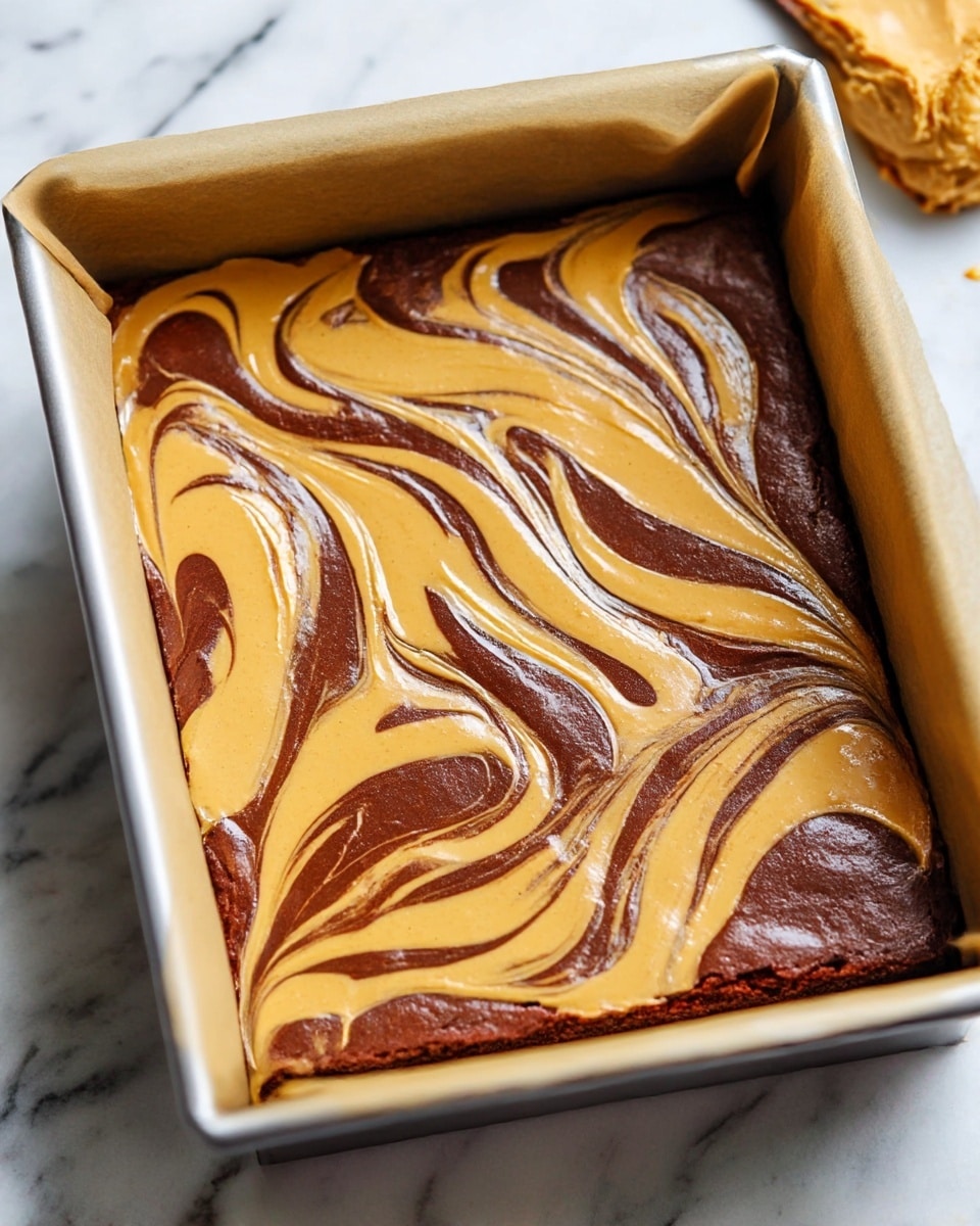 The image shows a baking tray lined with parchment paper, filled with a mixture that has two layers swirled together. The base layer is a rich, dark brown chocolate batter, smooth and glossy. On top, there is a golden peanut butter batter, which is swirled into the chocolate in large, flowing curves and loops, creating a marbled effect. The surface is shiny and slightly wet, ready to be baked. The tray is placed on a white marbled surface. photo taken with an iphone --ar 4:5 --v 7