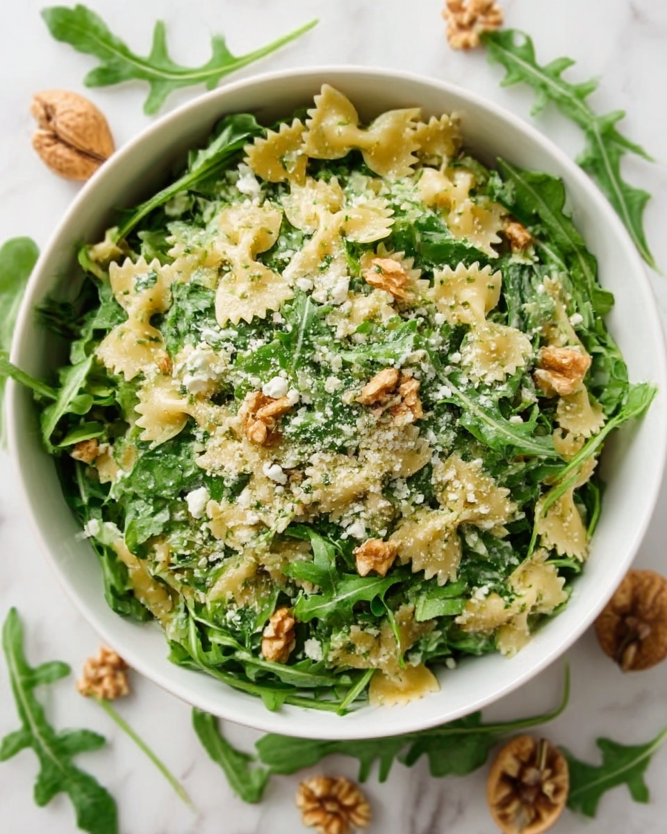 A white bowl filled with a fresh salad sits on a white marbled surface. The salad has three main layers: the bottom layer is a bed of dark green arugula leaves, the middle layer contains large pieces of light cream-colored ravioli pasta, and the top layer is sprinkled with small chopped walnuts and grated pale yellow cheese. The textures contrast between the soft pasta, crunchy nuts, and leafy greens. The colors are mainly green, cream, and brown. Photo taken with an iphone --ar 4:5 --v 7