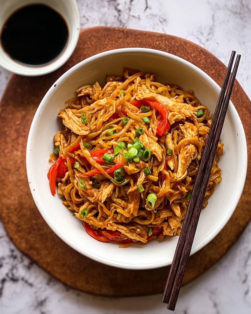 A close-up view of a black wok filled with cooked curly ramen noodles coated in a glossy reddish-brown sauce. Mixed throughout the noodles are small strips of light golden-brown cooked chicken, and bright green sliced chili peppers add a fresh contrast. A wooden spatula is lifting a portion of the noodles and chicken from the wok, showing the shiny, saucy texture and slight charring on some pieces. The background is a white marbled texture. photo taken with an iphone --ar 4:5 --v 7